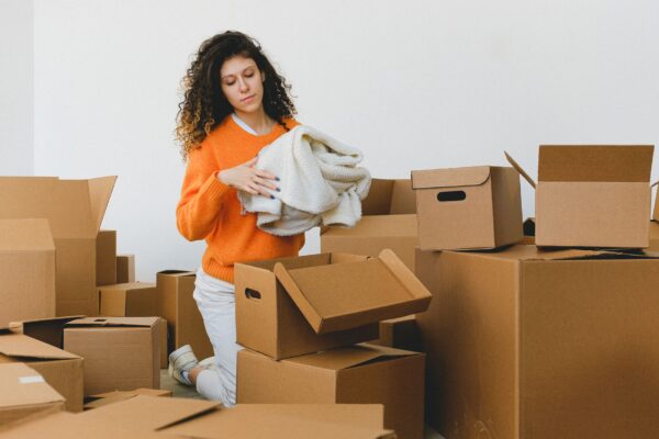Woman packing folded clothes into cardboard boxes before moving house