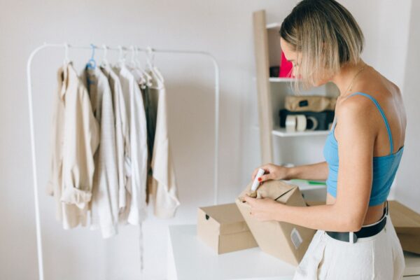 Woman packing clothes into a box beside a hanging clothes rail